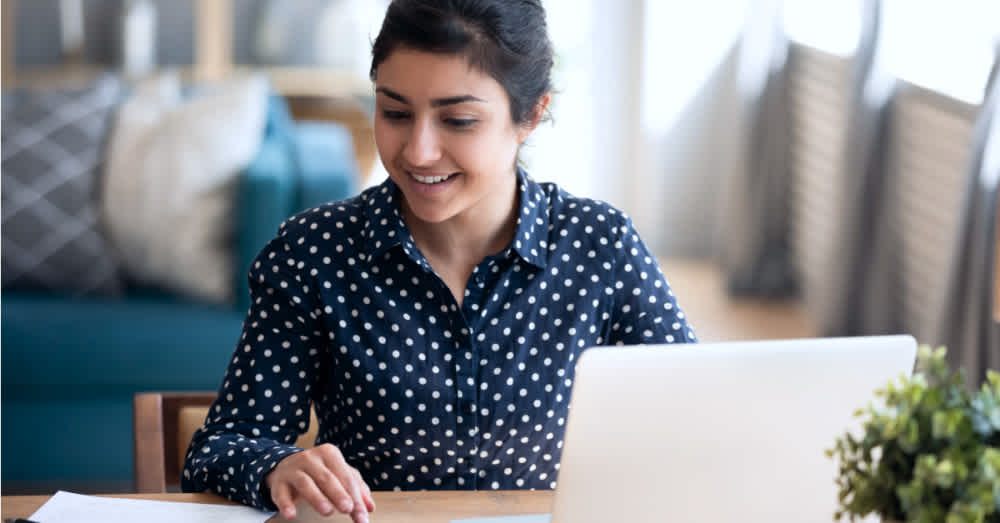 A woman in a polka dot shirt at her desk and reading her notepad